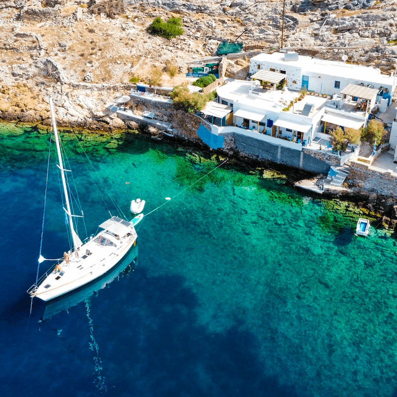 Aerial view of sailboat beside cliffside white houses in Greece