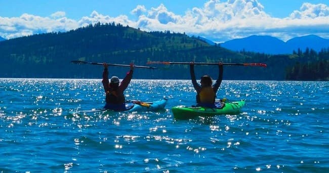 Two kayakers paddling on alpine lake with mountain backdrop