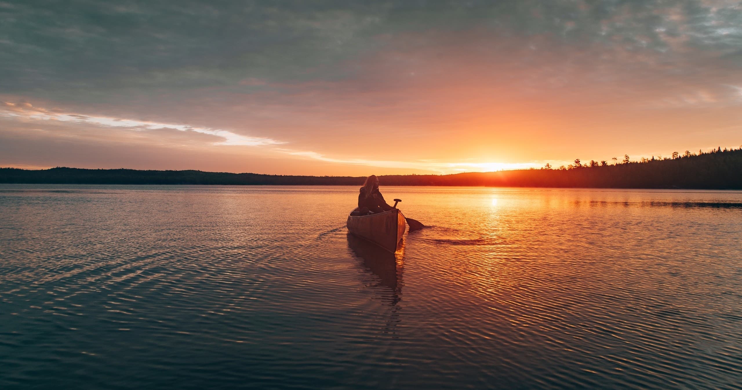 Kayaker silhouetted paddling at golden sunset on lake