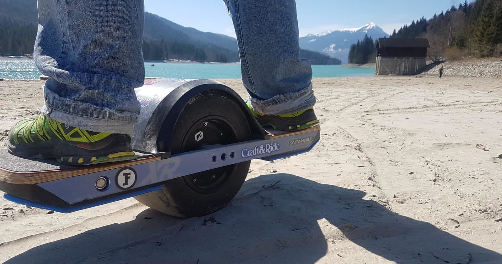 Electric one-wheel ride along sandy lakeshore with mountain views