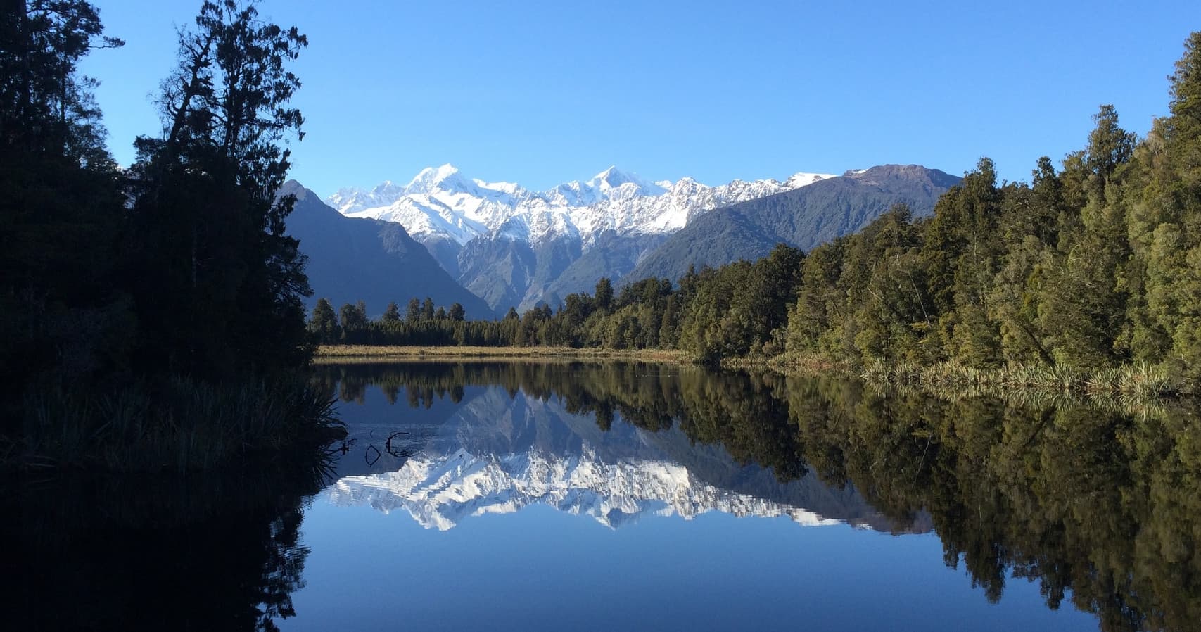 Reflective mountain lake with snow peaks, scenic hiking vista