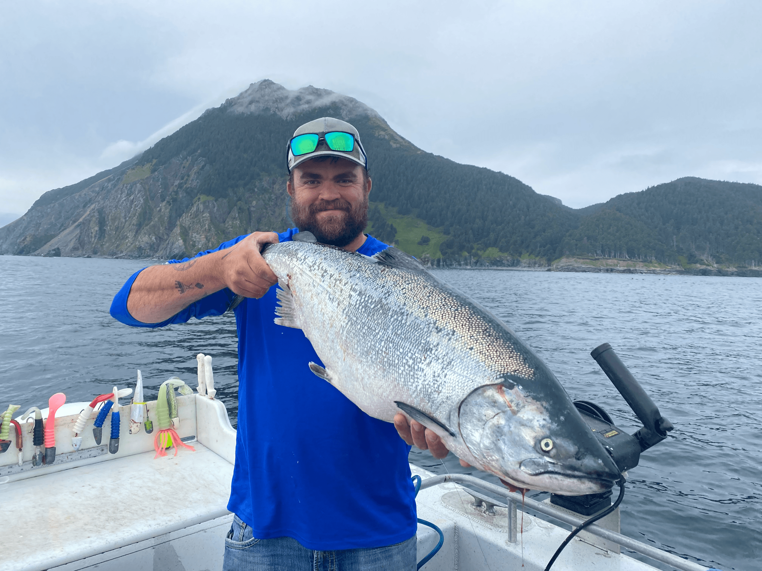 Angler holding large salmon on boat with coastal mountains