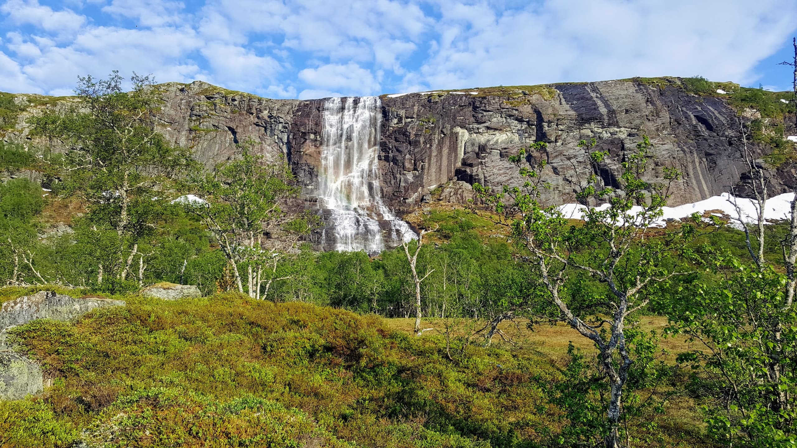 Waterfall cascading over rocky plateau amid green Norwegian tundra