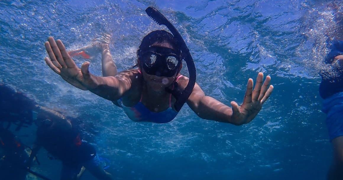 Snorkeler swimming underwater among coral and blue ocean in tropics