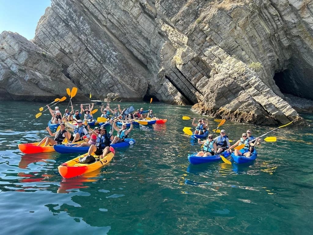 Group sea kayaking in crystal waters passing dramatic coastal caves