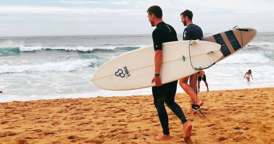 Surfers carrying surfboard on sandy beach with ocean waves