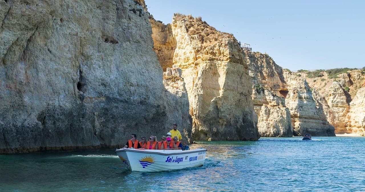 Small tour boat cruising turquoise sea past limestone cliffs
