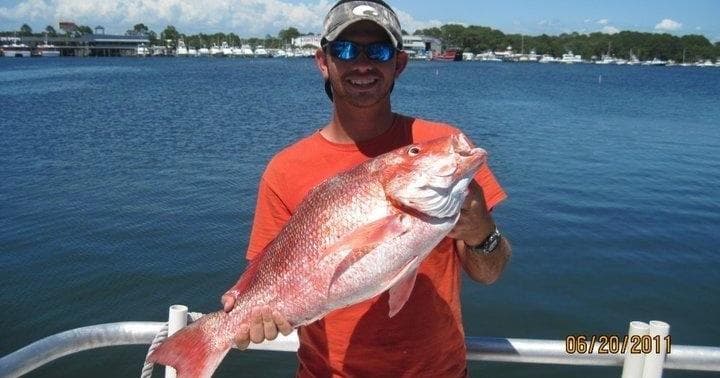 Angler holding red snapper on deck with ocean background