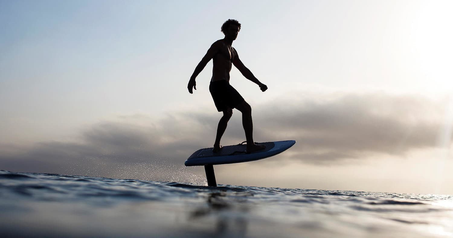 Silhouette e-foil rider gliding over open ocean at sunset