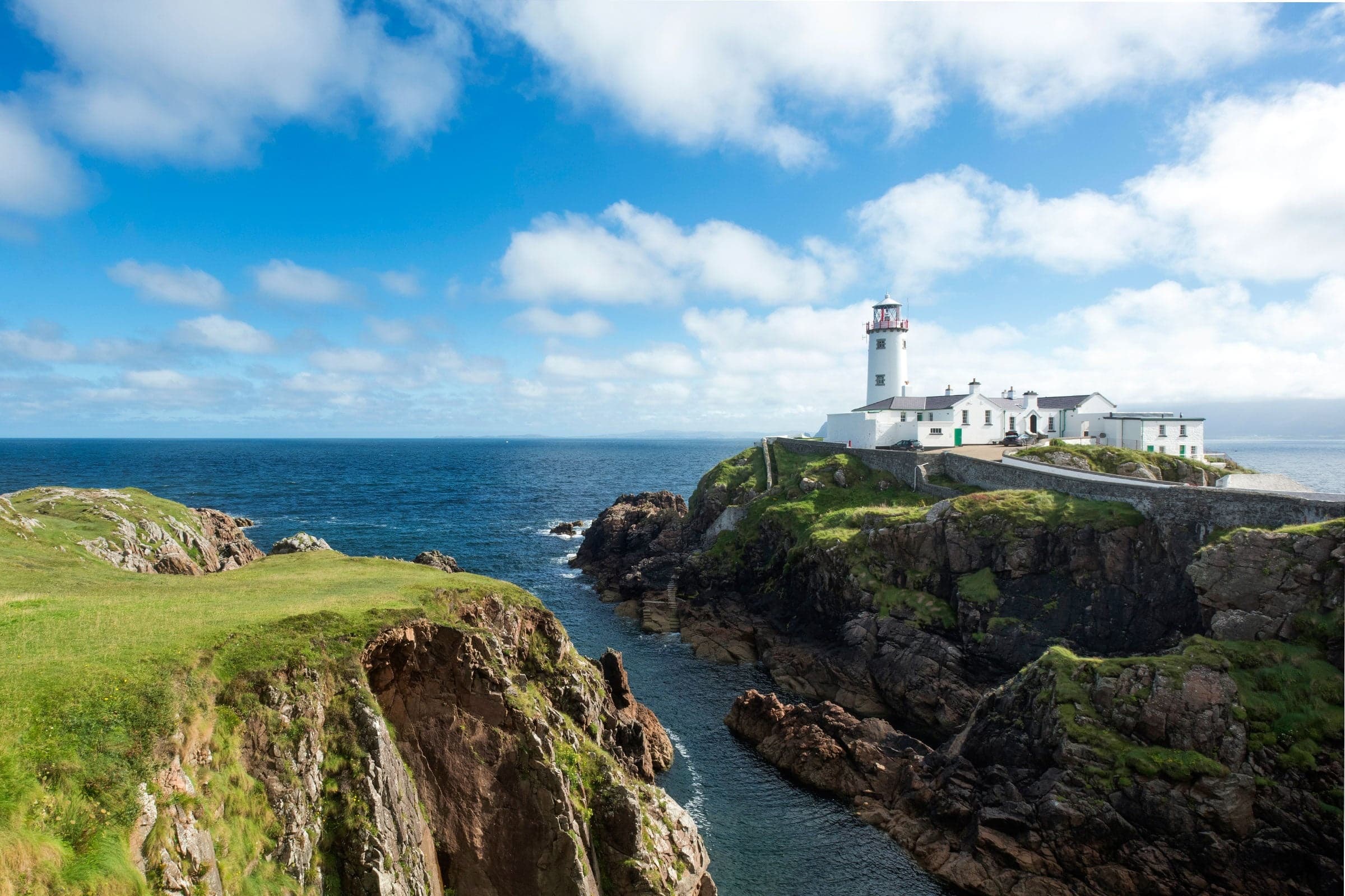 Lighthouse on rocky headland with kayakers and sea cliffs