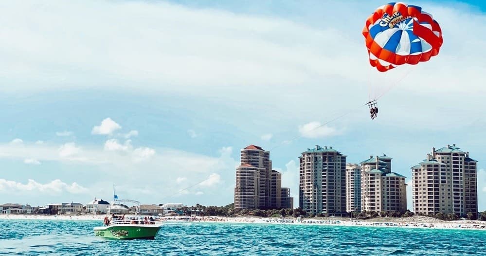 Parasailing over turquoise Gulf waters near beachfront skyline