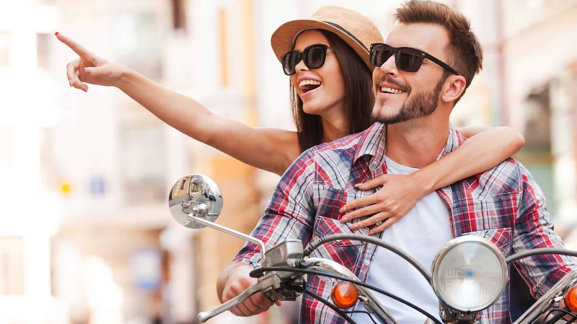 Happy couple riding scooter through sunny European city street