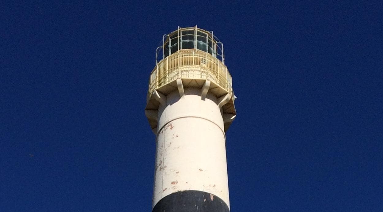Coastal lighthouse tower against deep blue sky overlooking ocean