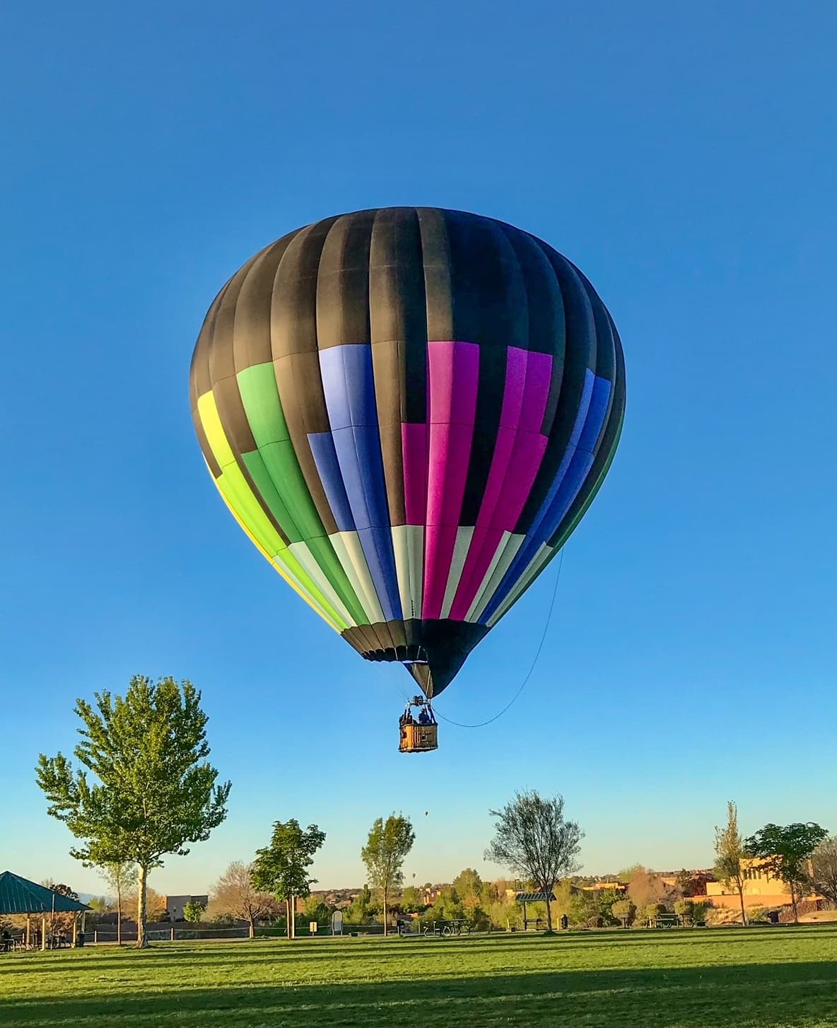 Single hot air balloon landing over suburban park at golden hour