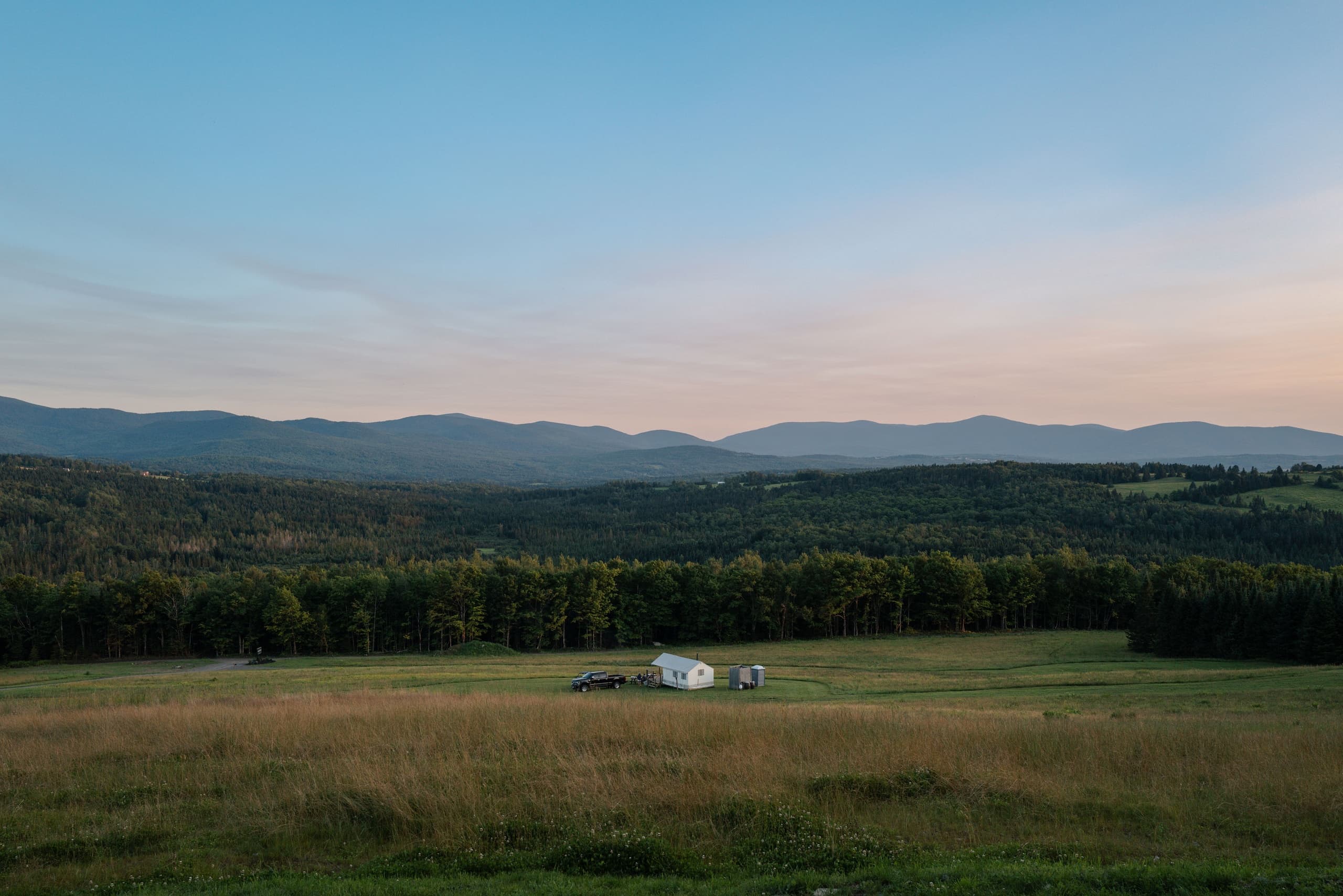 Panoramic mountain and meadow vista at sunset over farm