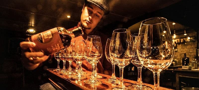 Bartender pouring tasters into wine glasses at dim pub counter