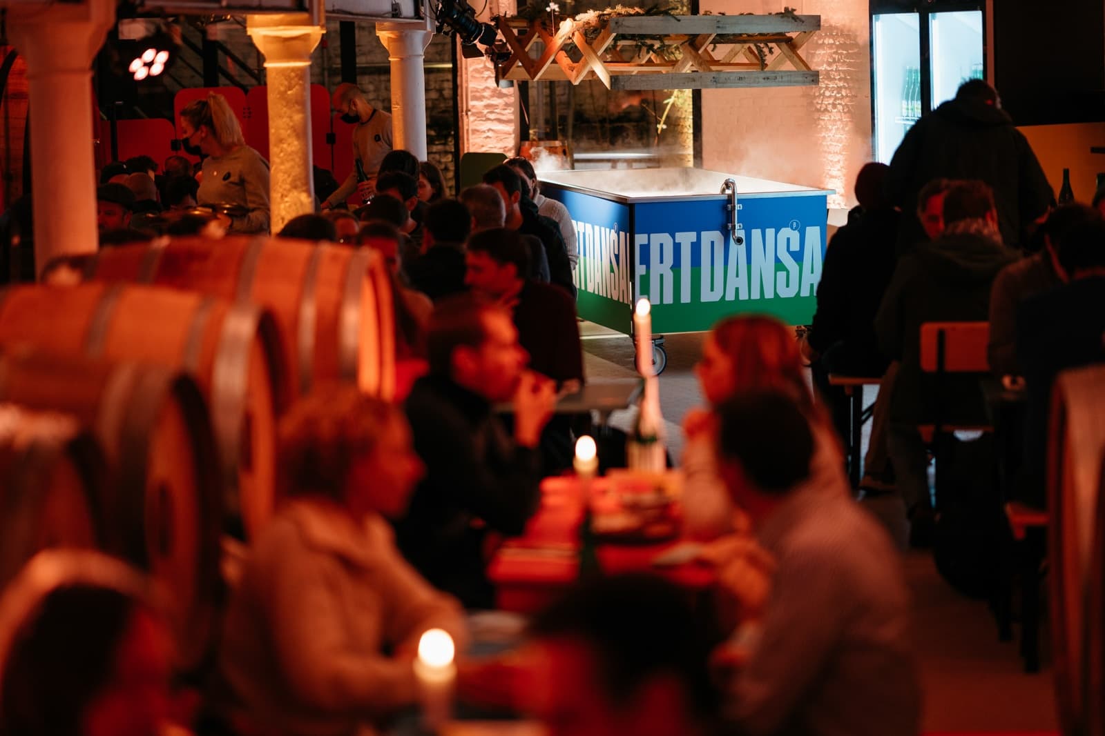 Dimly lit brewery dinner service among oak barrels and diners