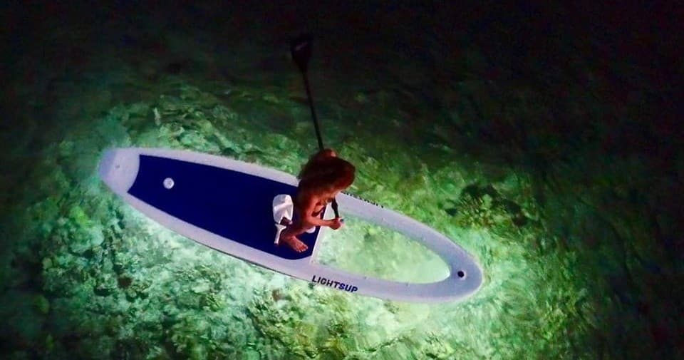Overhead night paddleboarding with illuminated board over reef