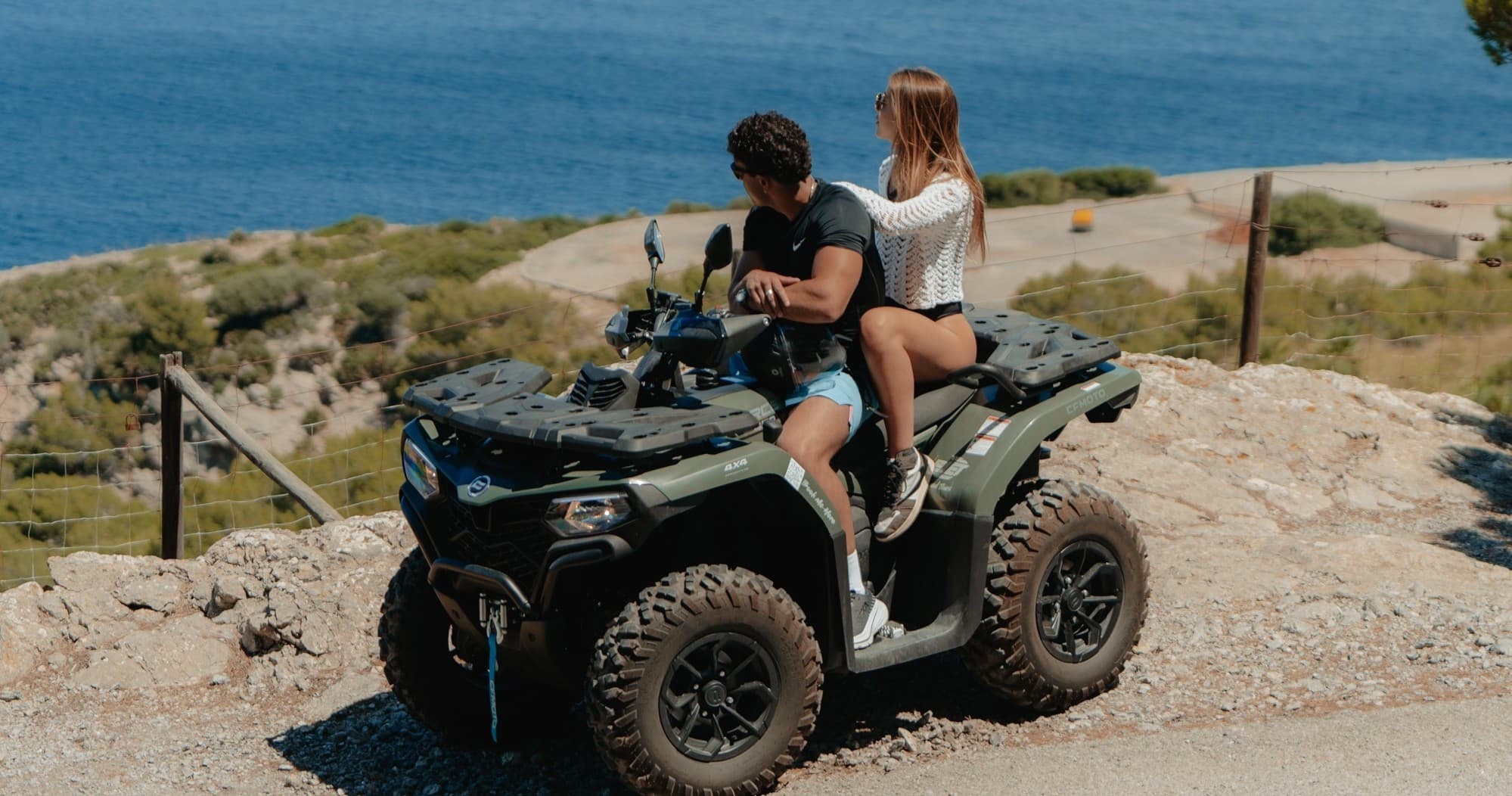 Couple riding ATV along coastal cliff road overlooking sea