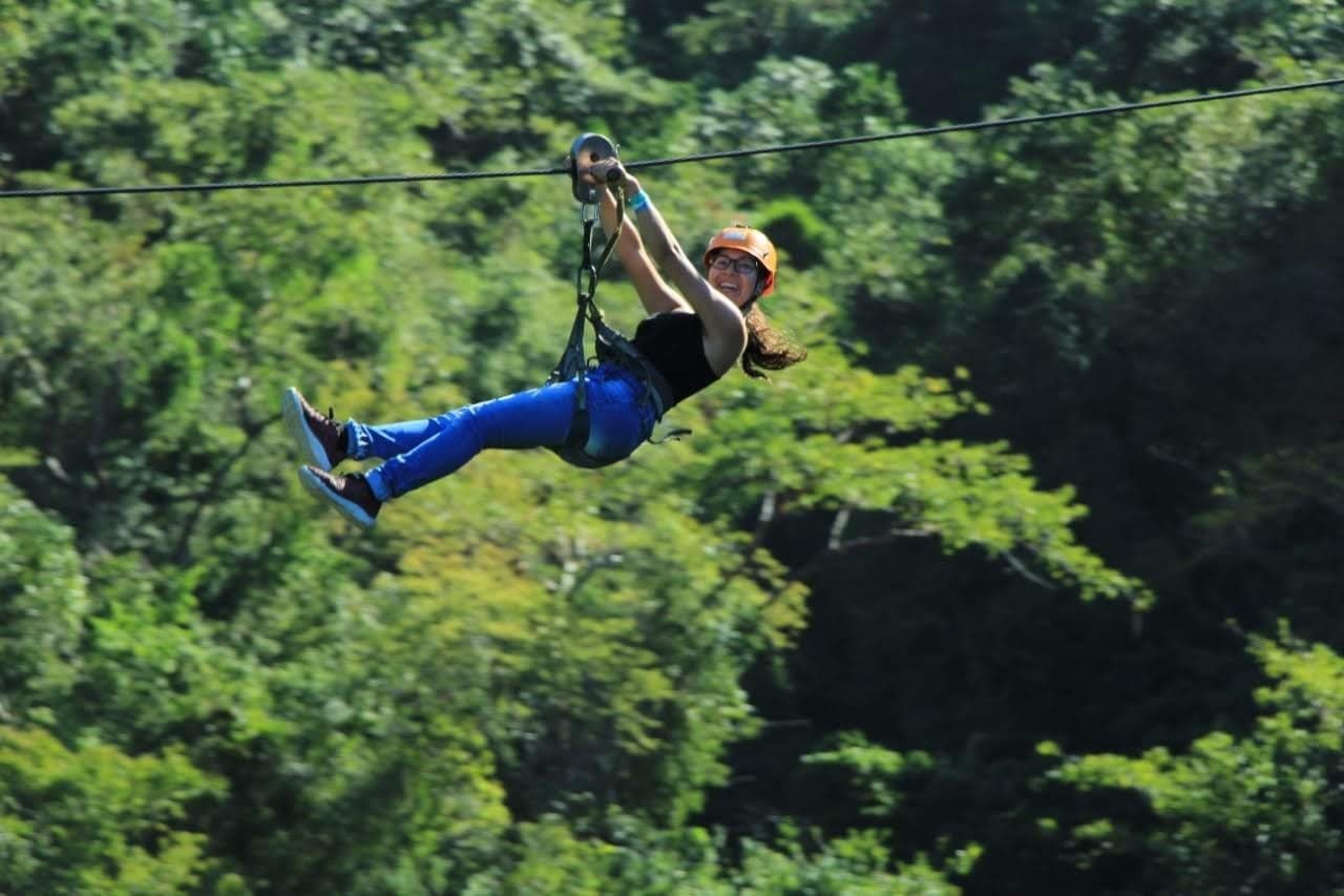 Zipline rider gliding over lush tropical forest canopy
