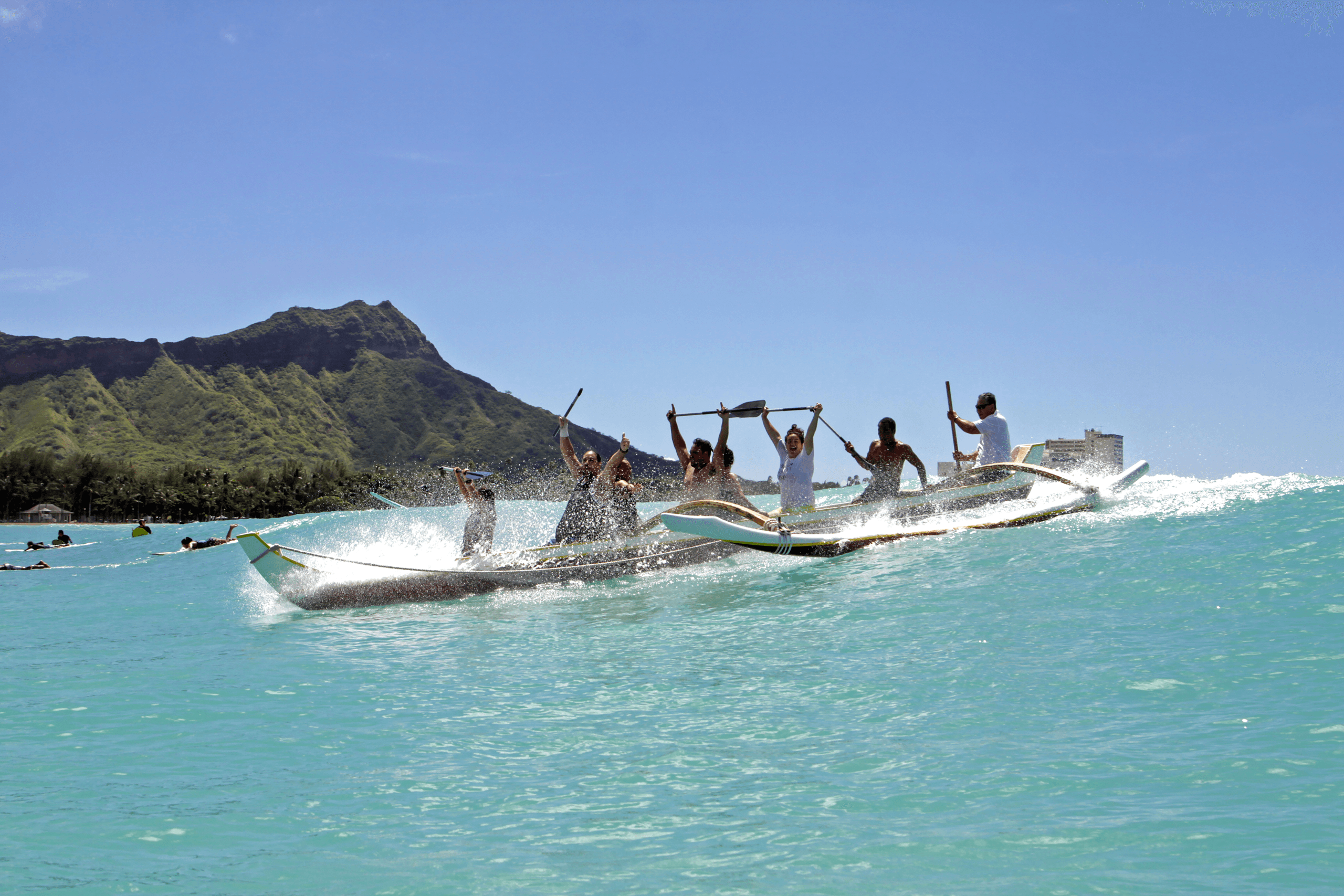 Outrigger canoe crew racing across clear turquoise ocean at Waikiki