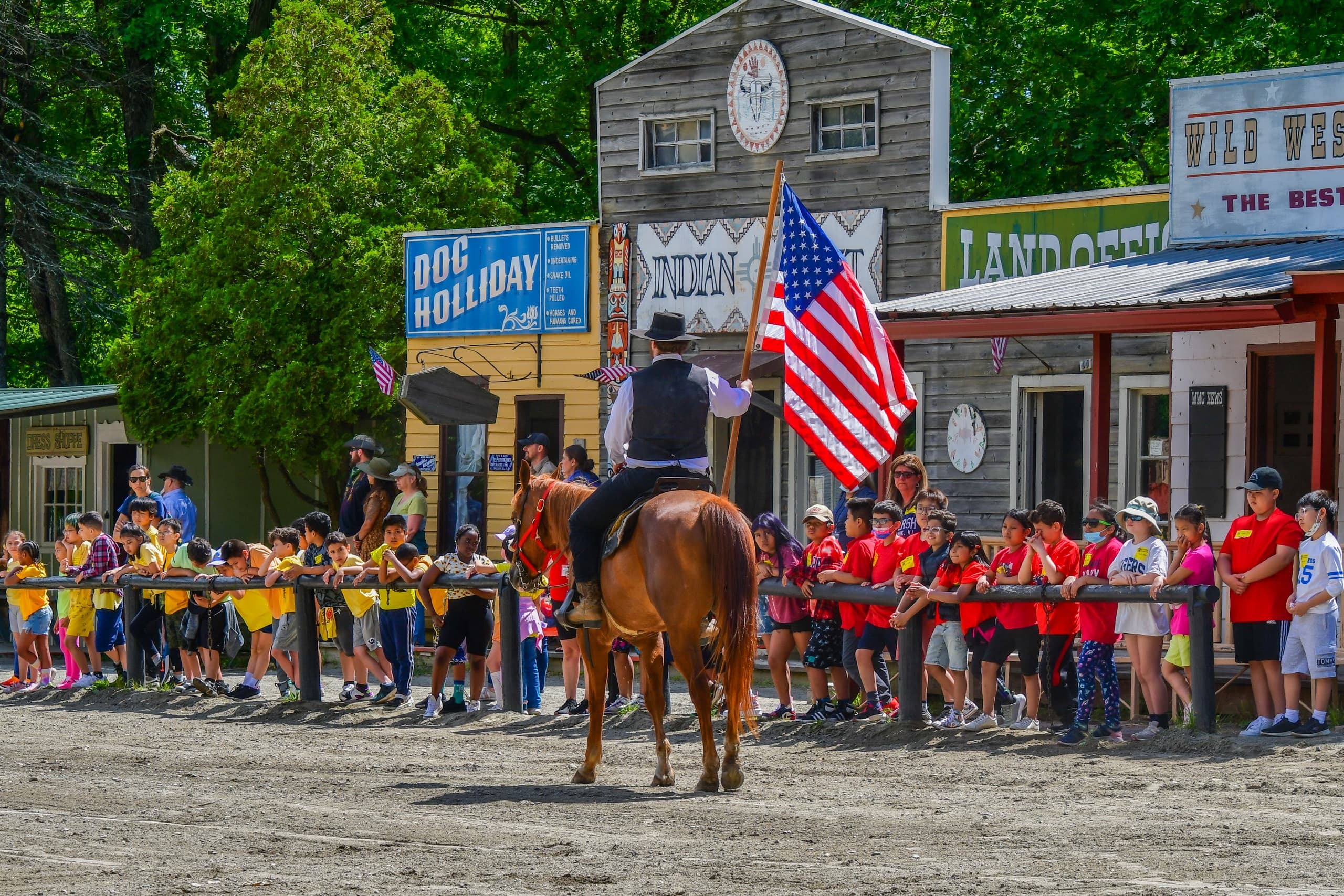 Crowd watching mounted rider carrying American flag at Wild West town parade