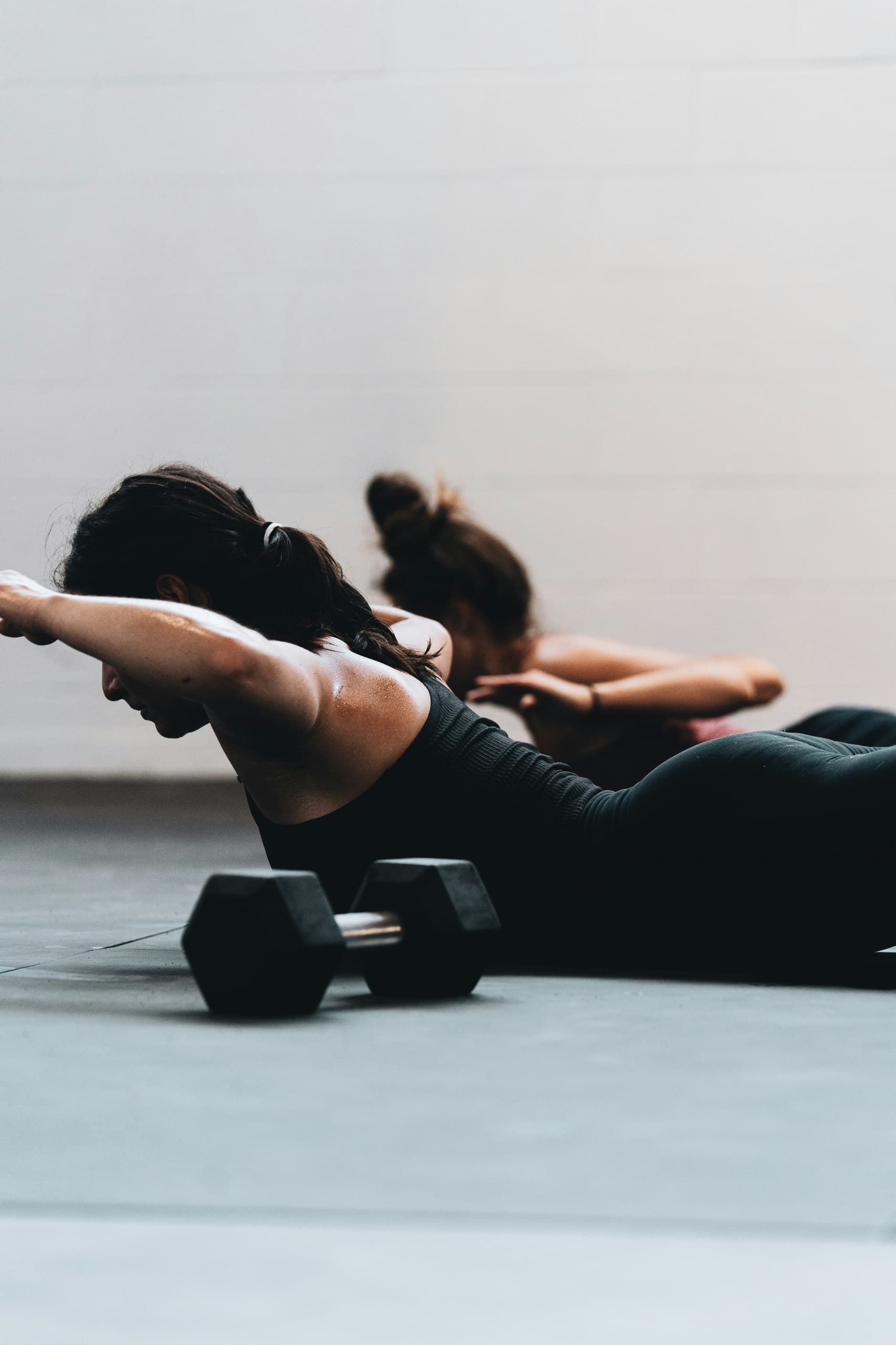 Women doing back extensions with dumbbells in indoor gym class