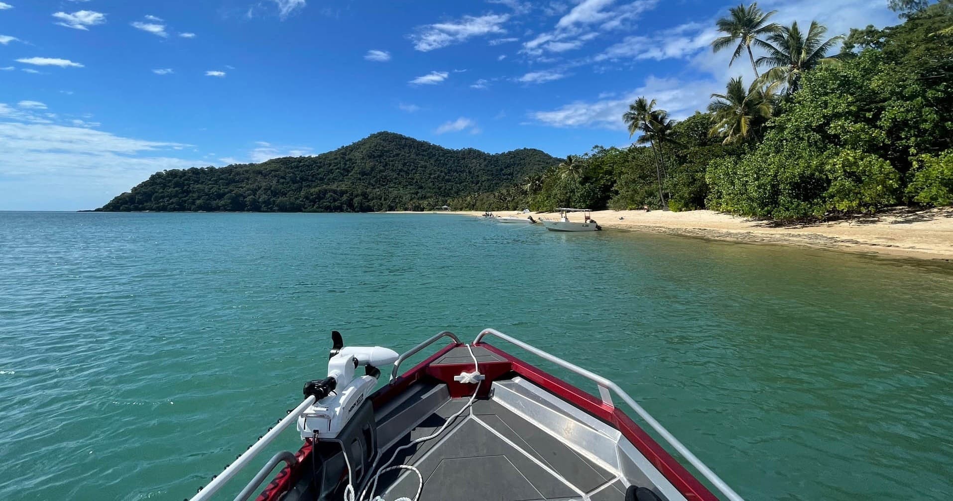 Fishing boat bow heading toward tropical island beach, turquoise sea