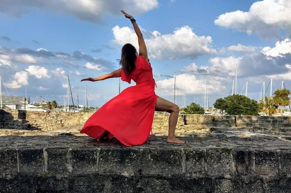 Dancer in red performing on coastal ruins with blue sky