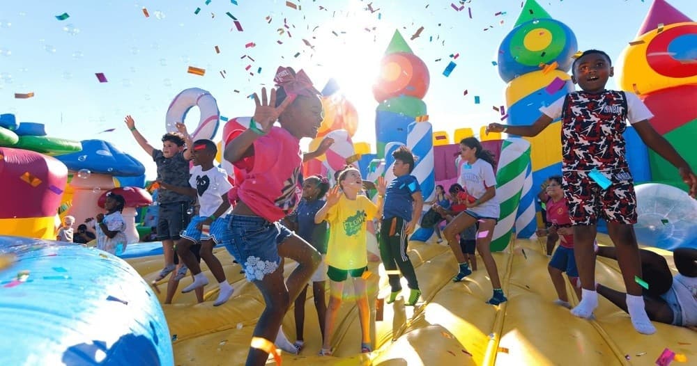 Families celebrating on outdoor bouncefield with confetti and sun