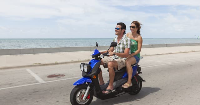 Couple riding blue scooter along coastal road with ocean view