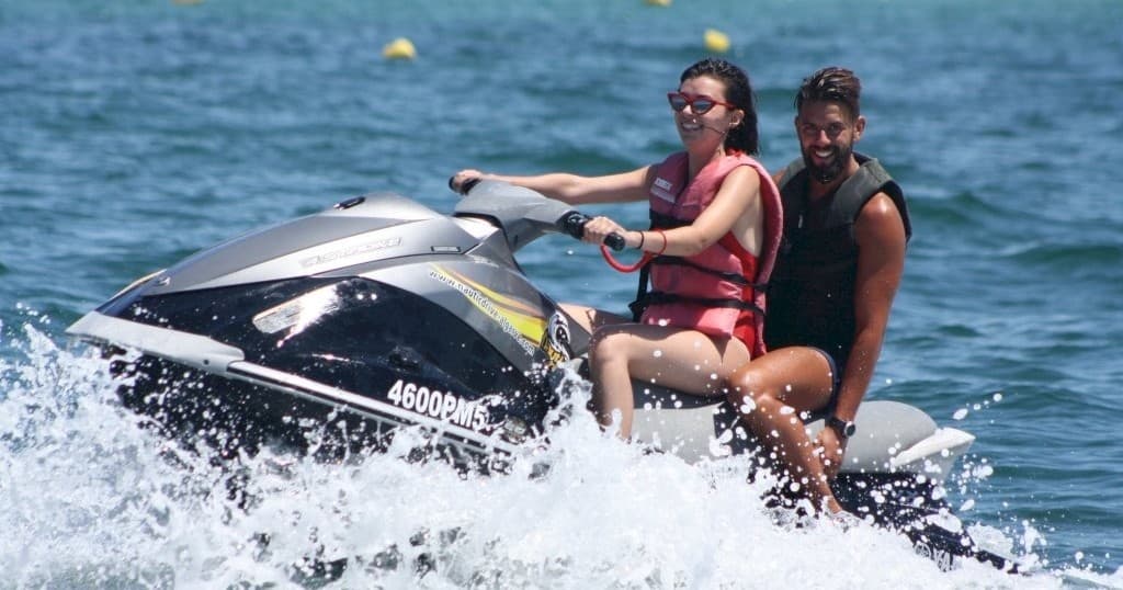 Two riders on a jet ski speeding across blue coastal waters
