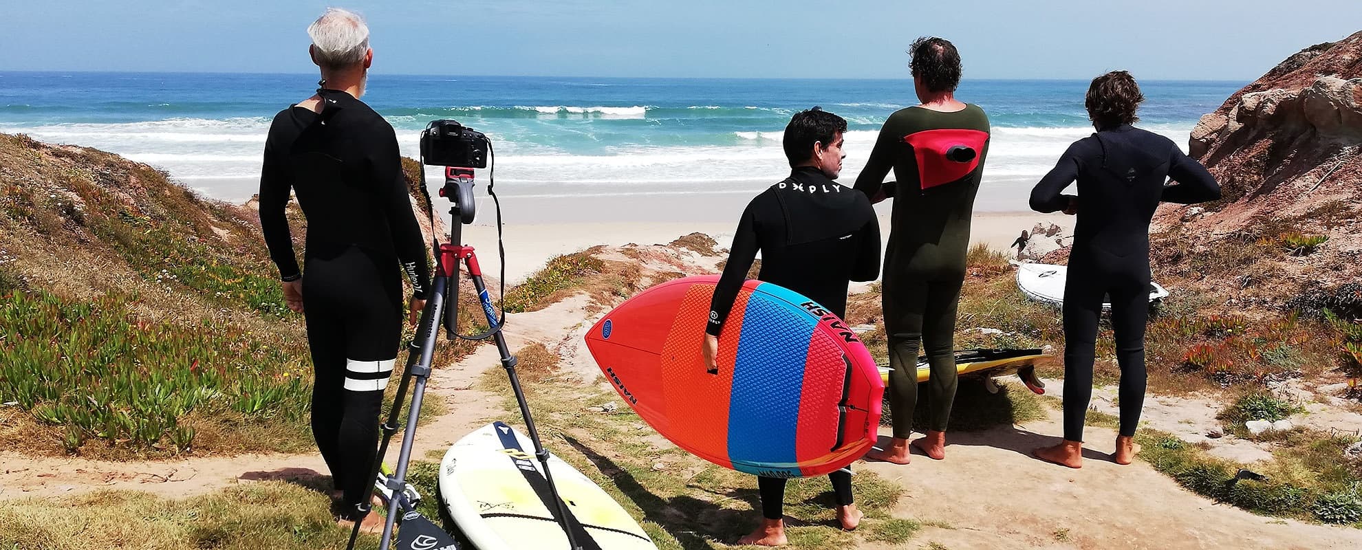 Surfers carrying colorful boards toward ocean across dunes