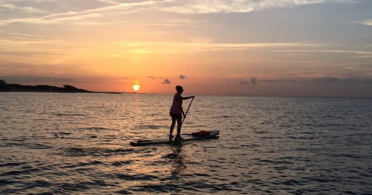 Paddleboarder silhouetted at sunset on open coastal waters