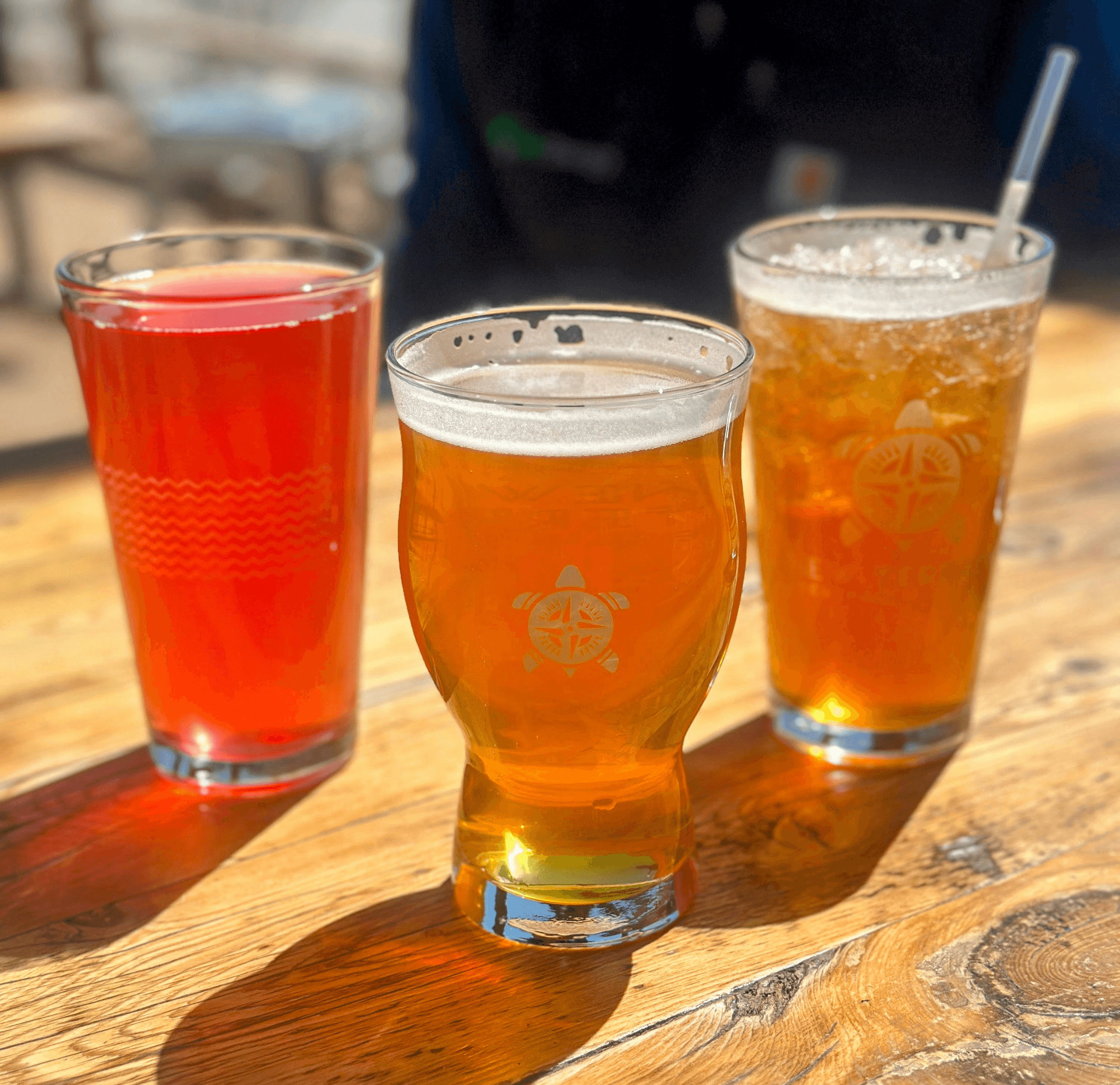 Three craft beers on wooden patio table at sunny brewery