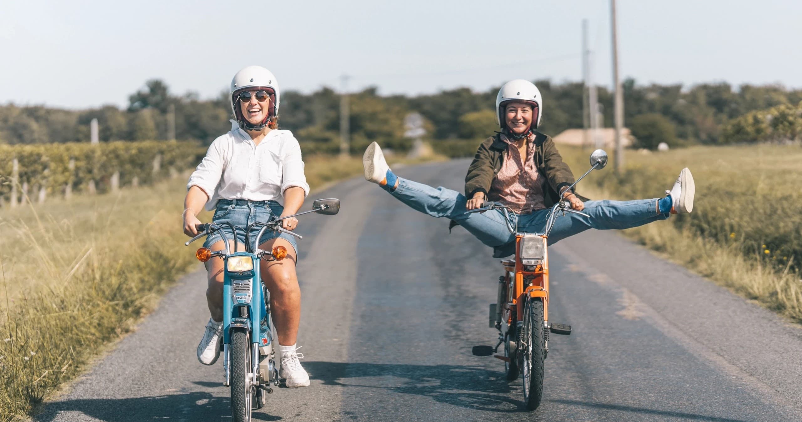 Two riders on vintage mopeds on rural road enjoying scenic ride