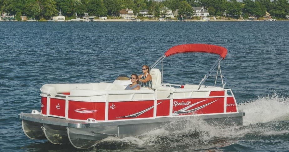 Red pontoon boat cruising on open lake near shoreline cottages
