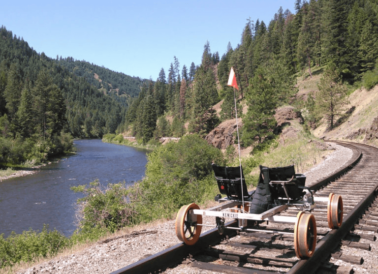 Two-person railbike on riverside tracks through pine forest canyon
