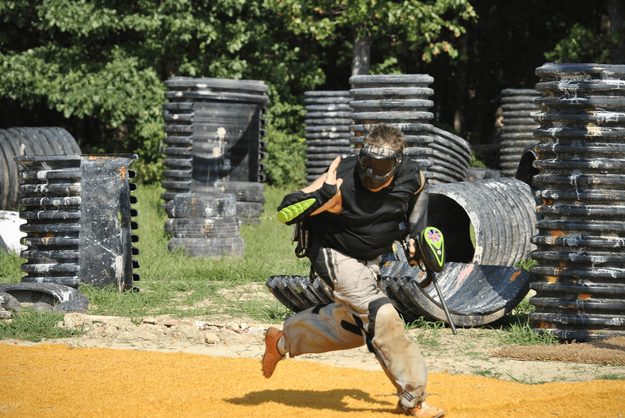 Player sprinting across outdoor paintball field among bunkers