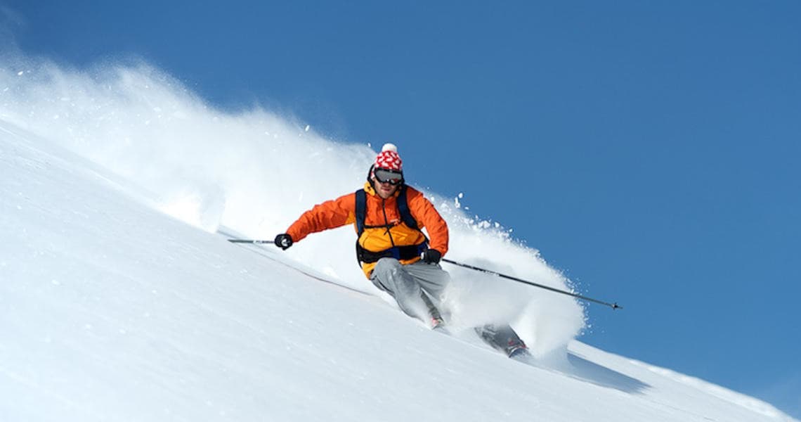 Skier carving fresh powder slope against bright blue alpine sky