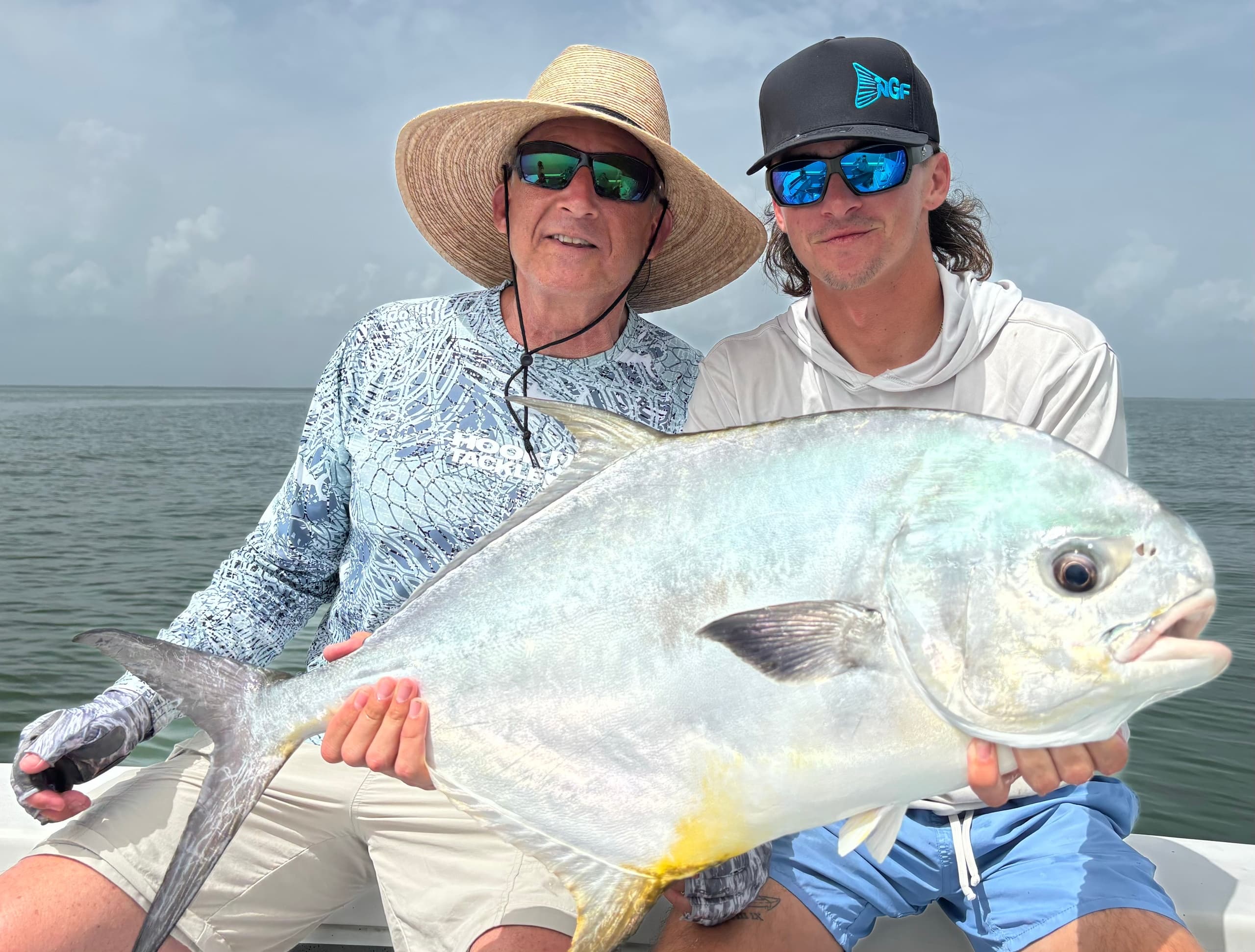 Two anglers holding large permit fish on boat, inshore saltwater fishing