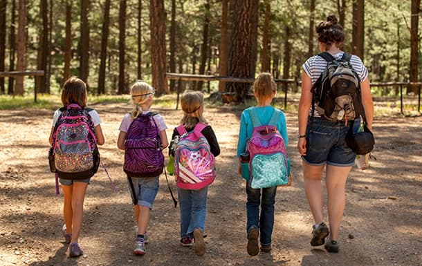 Children hiking on forest trail with leader in pine woods