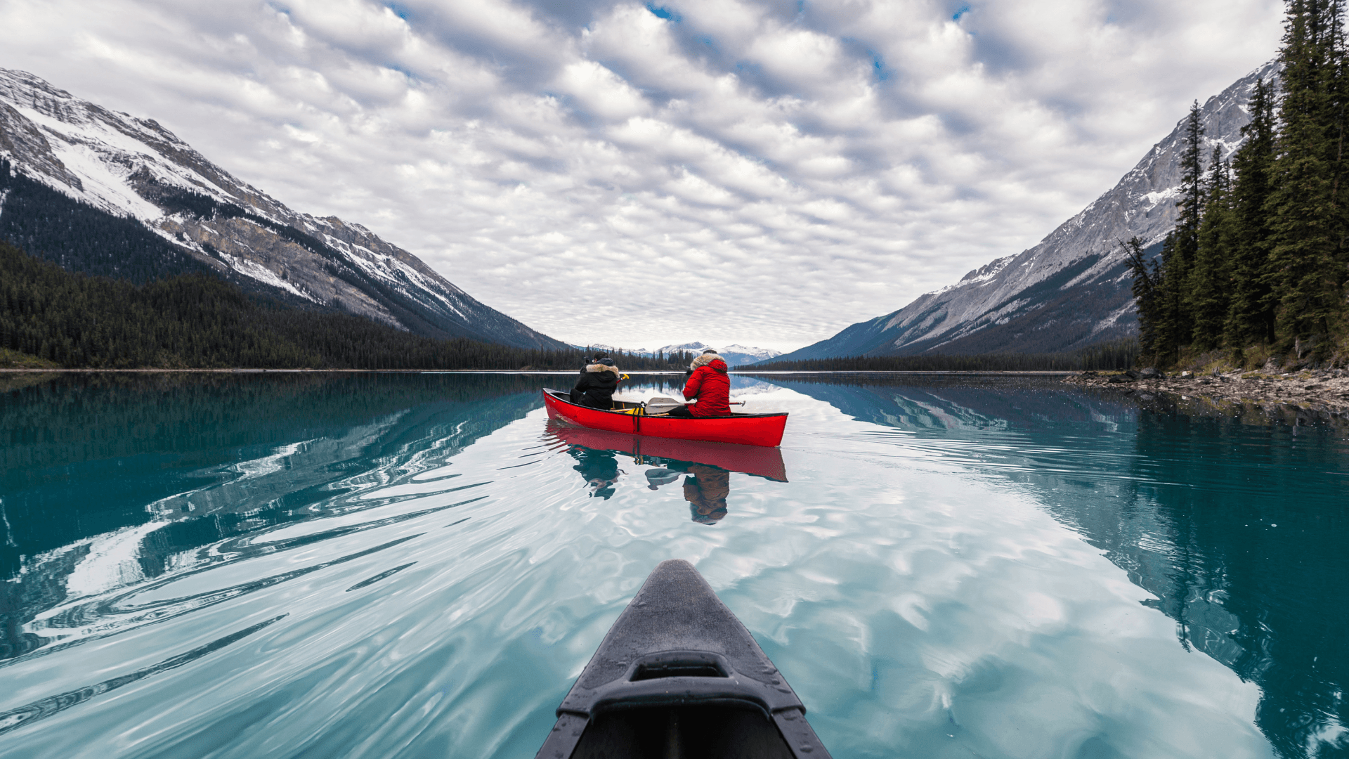 Red canoe centered on glassy mountain lake with cloud reflections