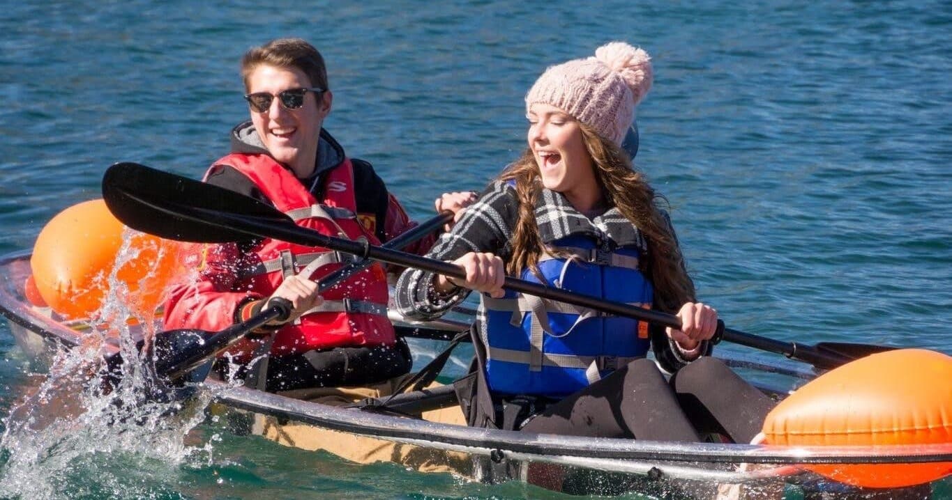 Couple paddling clear kayak on alpine lake, laughing
