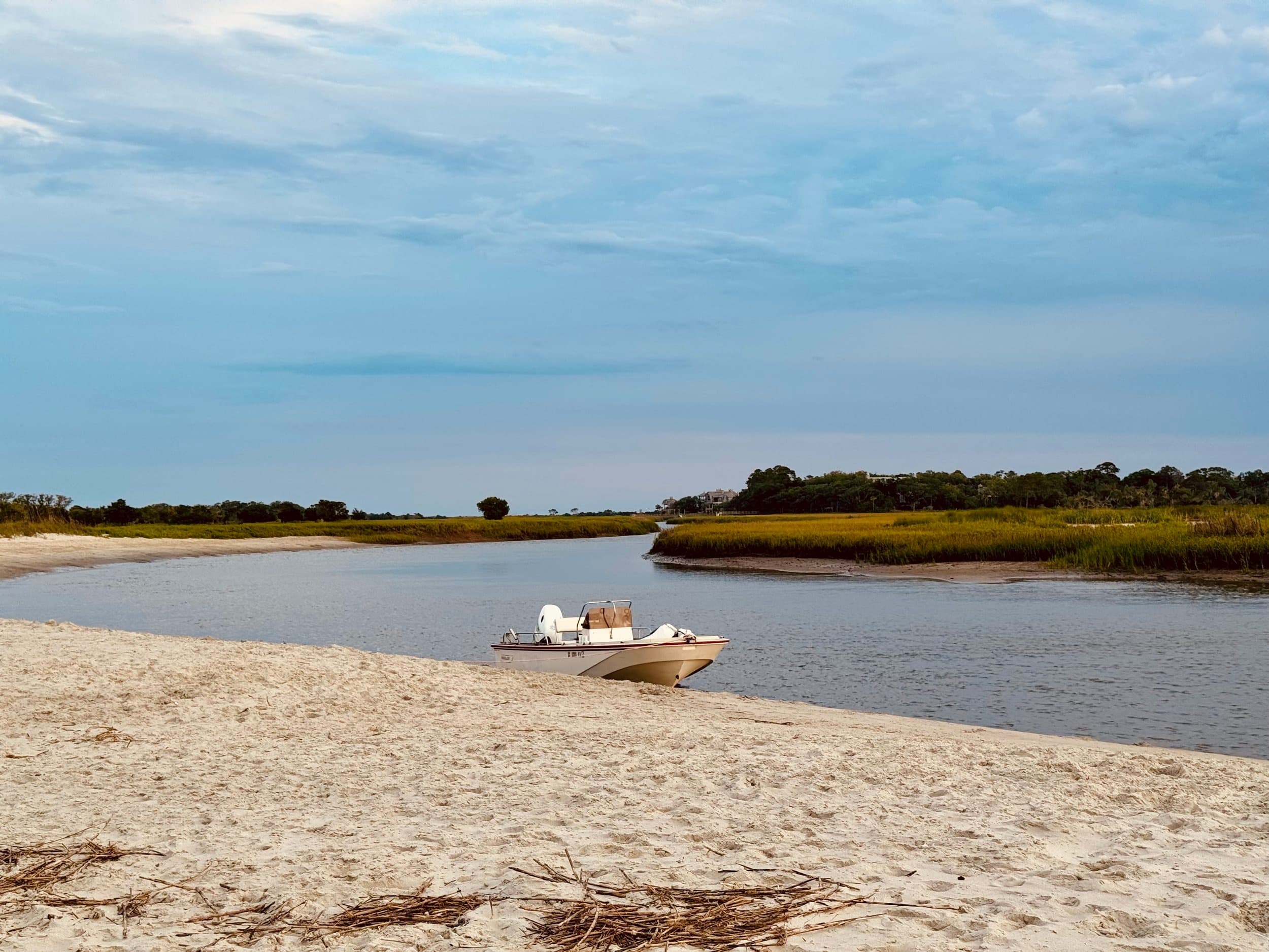 Small motorboat beached on sandy shore beside quiet marsh inlet