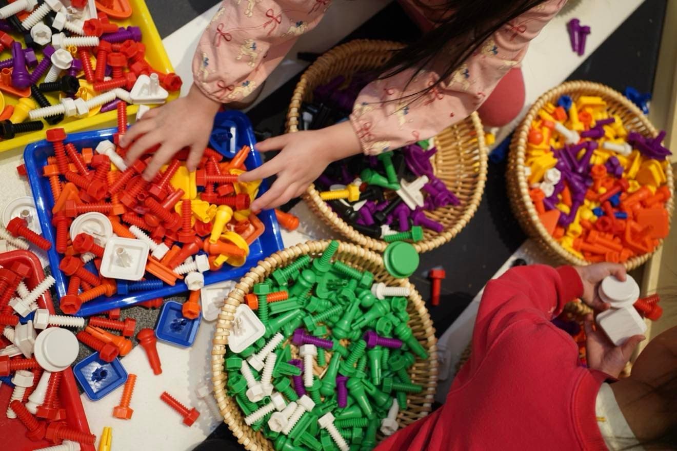 Kids sorting colorful craft pieces at indoor art studio table