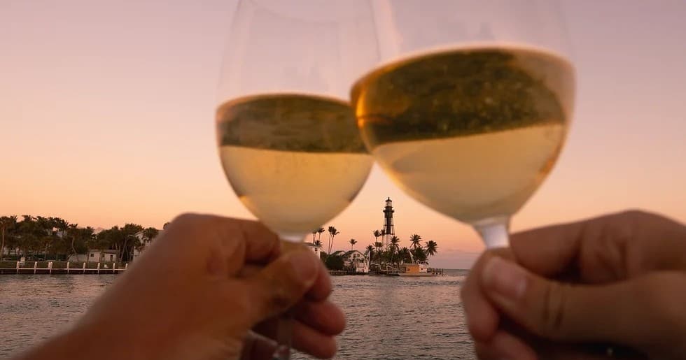 Couple toasting white wine at sunset on coastal boat with lighthouse