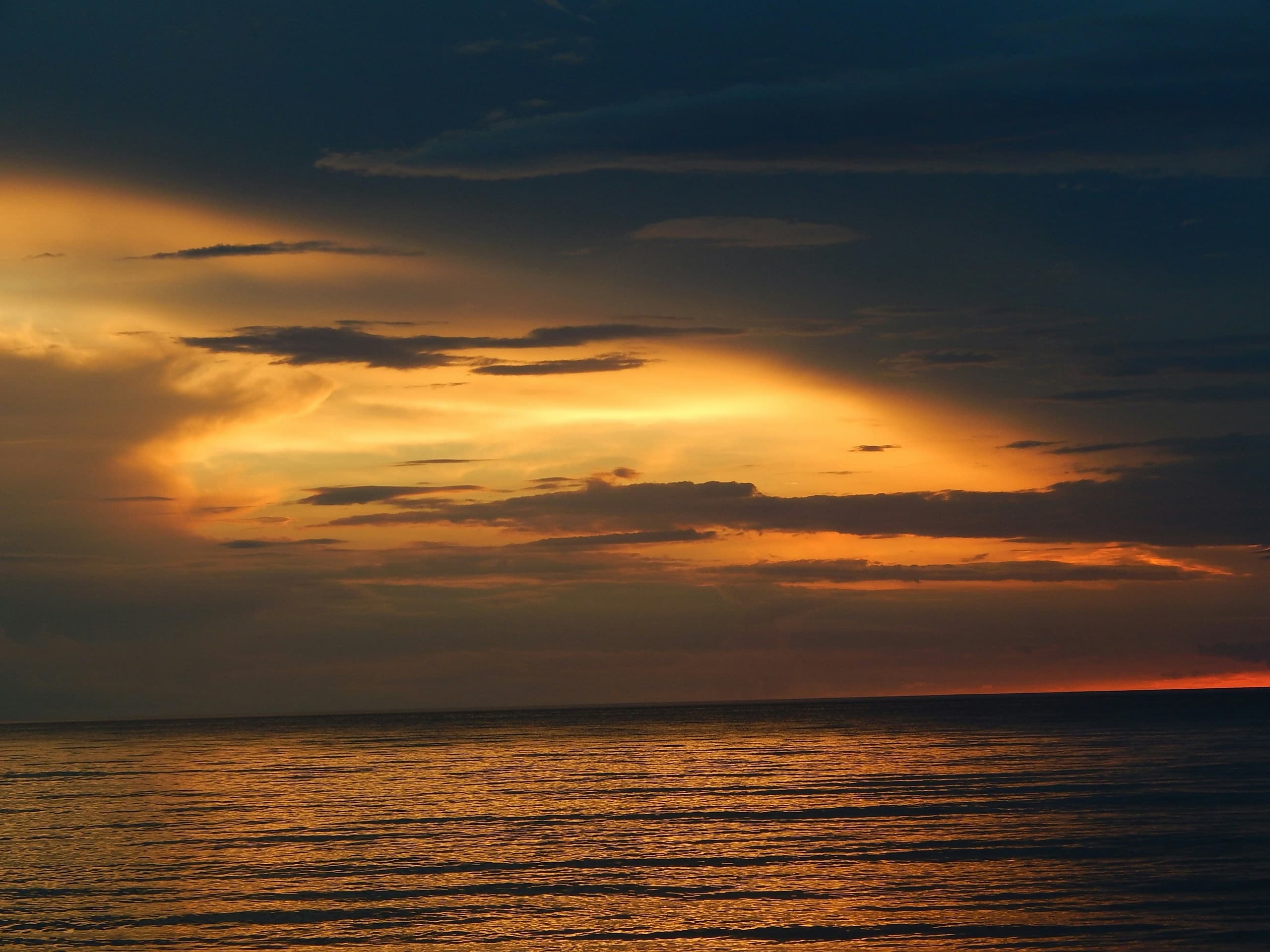 Dramatic sunset over open ocean with golden clouds, scenic shore cruise