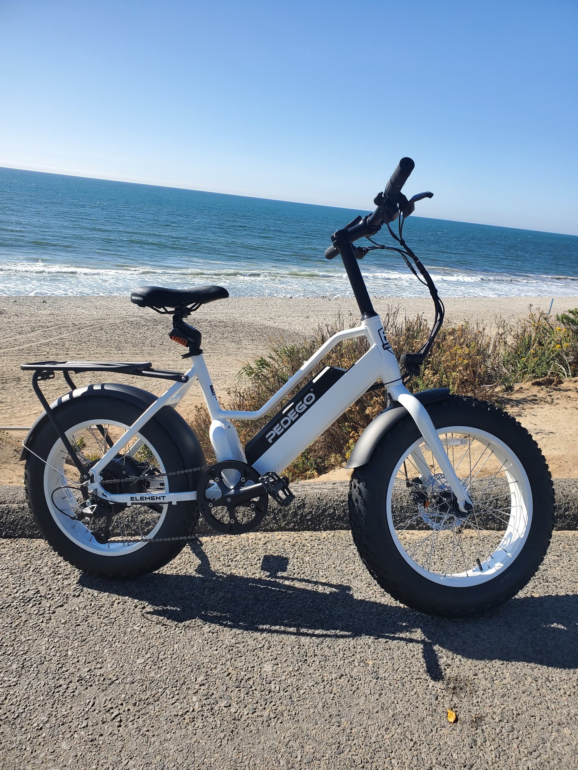 White electric bike parked on sandy beach with ocean view