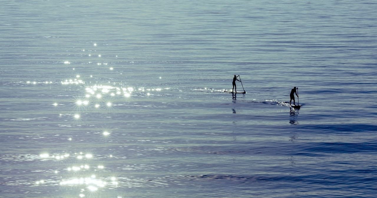 Two paddleboarders gliding on sunlit lake with sparkling water